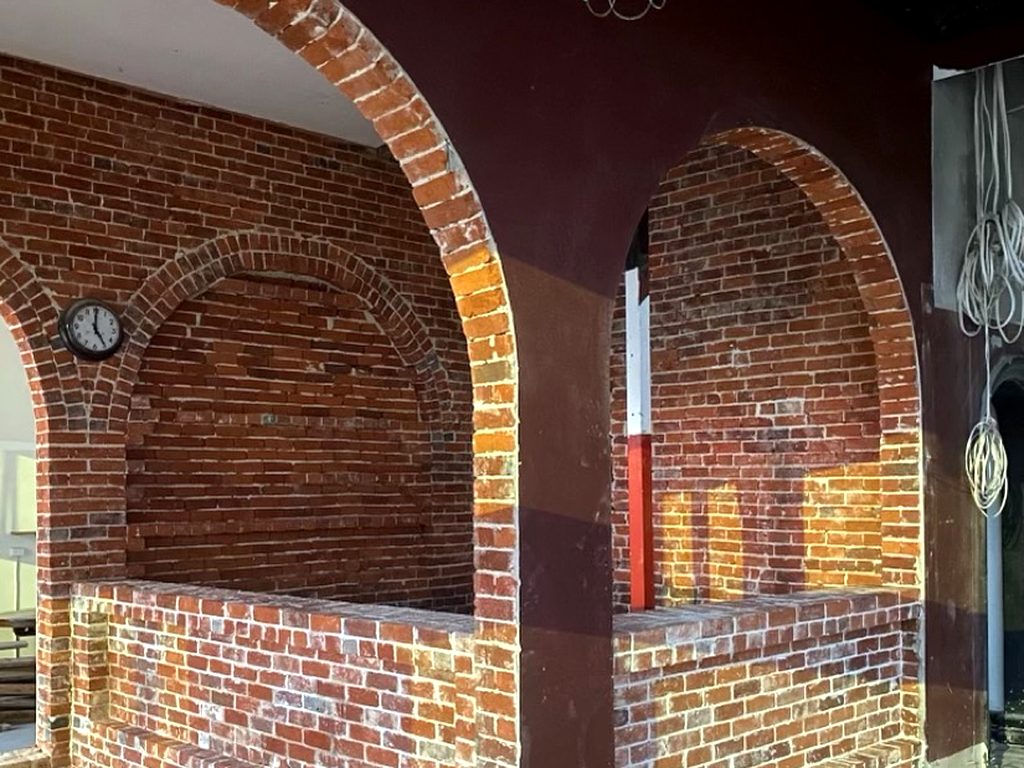 Twin brick archways inside the building, with an old wall clock and deep red painted walls above bare brickwork